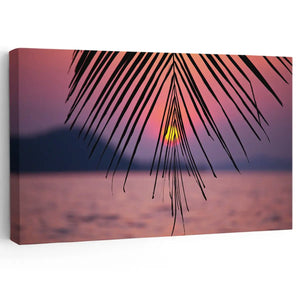  Large beach wall art featuring a serene sunset framed by palm tree leaves over a peaceful ocean view.

