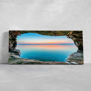 Large wall art ocean scene capturing a peaceful natural cave window with ocean reflections at sunset.