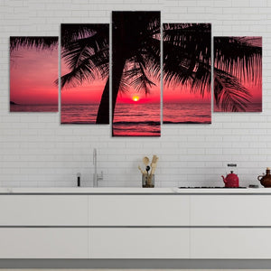 Large wall art ocean scene capturing a vivid red and pink sunset over calm ocean waves with palm trees